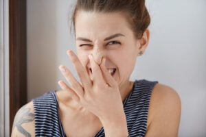 woman pinching her nose after turning on heater and smelling a stink bad odor